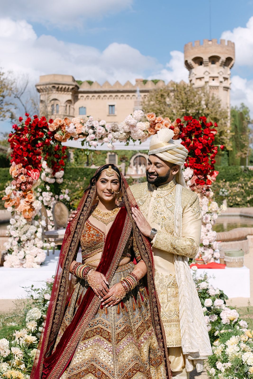 Indian bride and groom at a floral mandap in front of a castle