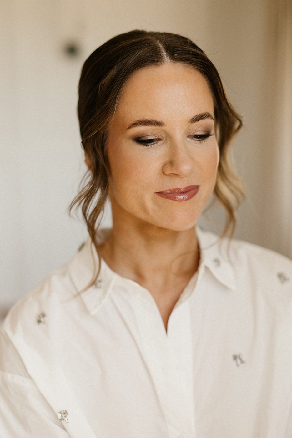 Bride with shimmer eye makeup and glossy lip, eyes lowered, in a white shirt